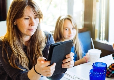 Women sitting at a table and looking at a tablet while sitting next to her daughter